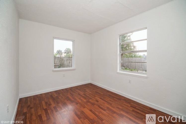 Empty room with wooden floors and two windows.