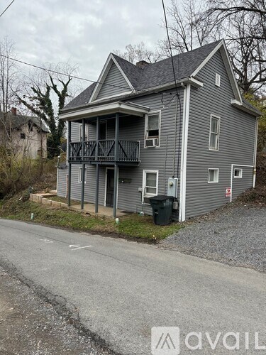 A grey house with a balcony and a trash can in front.