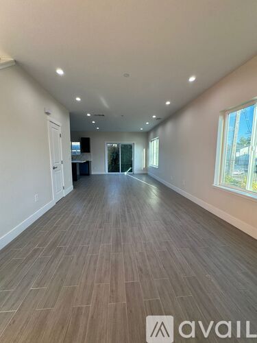 A spacious room with wooden flooring and a large window on the right side.