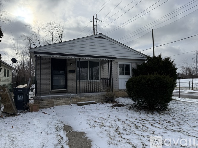 A house with a grey roof and a small porch is surrounded by snow.