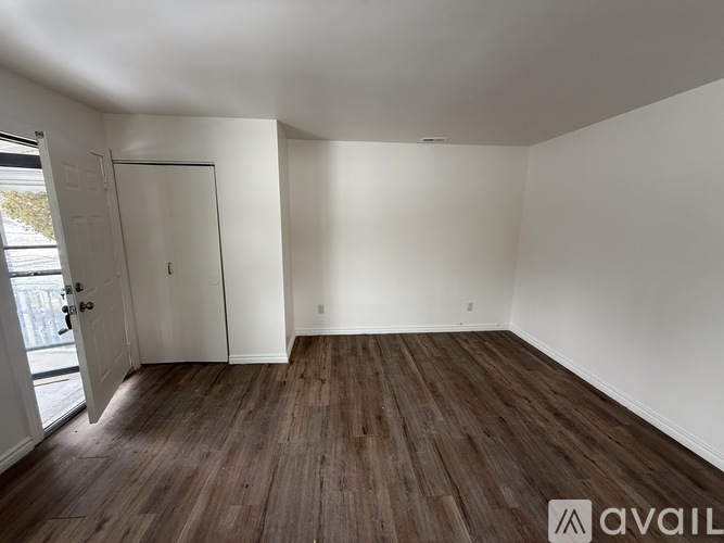 A room with wooden flooring and white walls, with a door on the left side.