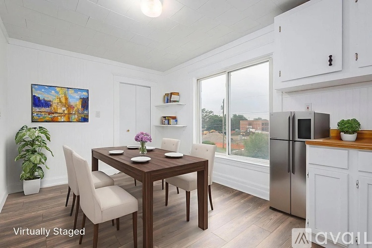 A dining room with a table set for two, a potted plant, and a painting on the wall.