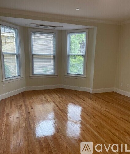 A room with wooden flooring and three windows.
