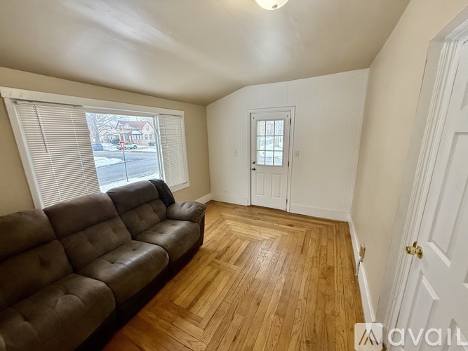 A living room with a brown leather couch and wooden flooring.