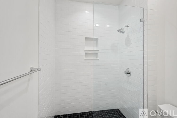 A white tiled shower with a glass door and a black mat on the floor.