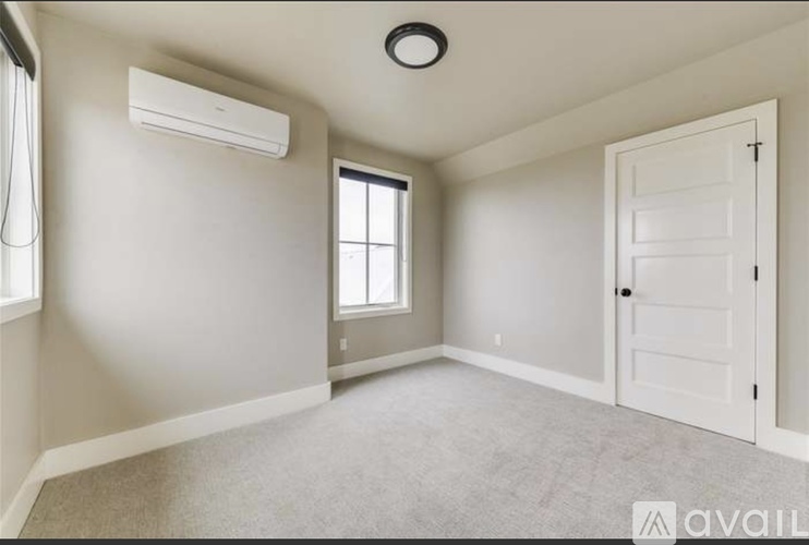 A spacious room with a window, carpeted floor, and a closed door.