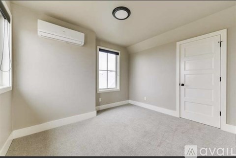 A spacious room with a window, carpeted floor, and a closed door.