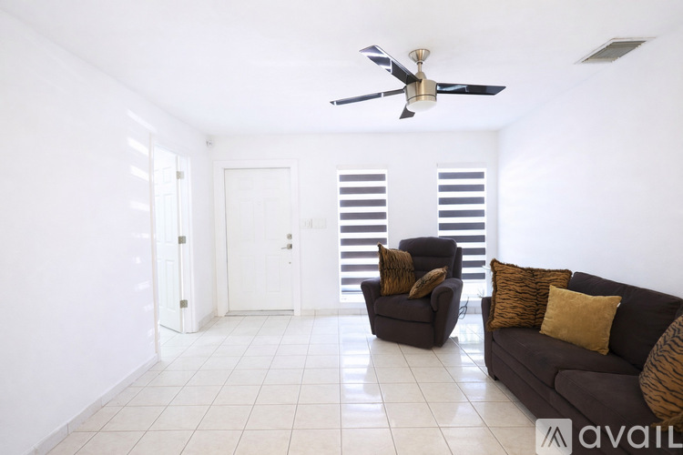 A living room with a brown couch, a fan, and a chair.