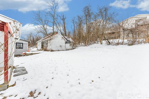 A snowy landscape with a house and bare trees.