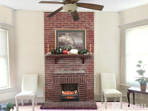 A fireplace with a painting above it and a fan above the fireplace.