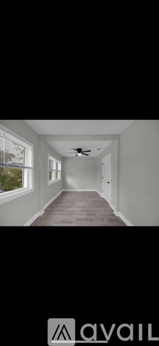 A long, empty hallway with a ceiling fan and windows on the left side.