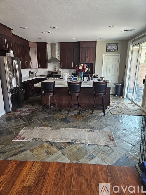 A kitchen with a refrigerator, bar stools, and a rug on the floor.