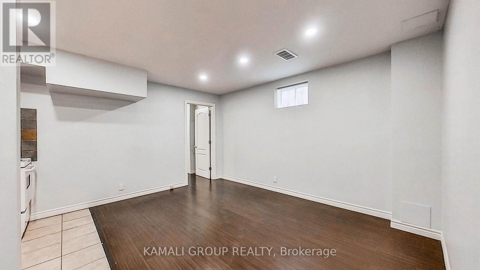 A spacious room with a wooden floor and white walls, with a window on the right wall.