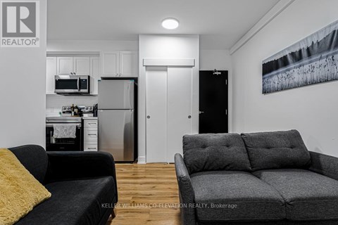 A living room with a grey couch and a black fridge.