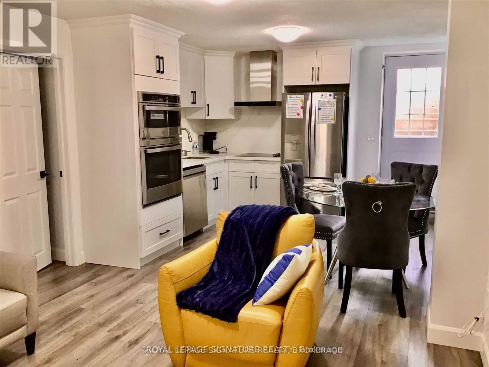 A yellow chair with a blue pillow is in the foreground of a kitchen.