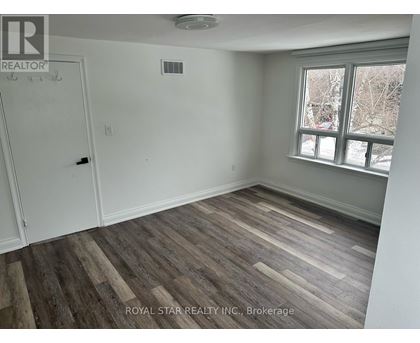 A room with wooden flooring and a window showing a view of trees and a building.
