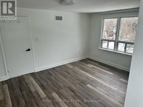 A room with wooden flooring and a window showing a view of trees and a building.
