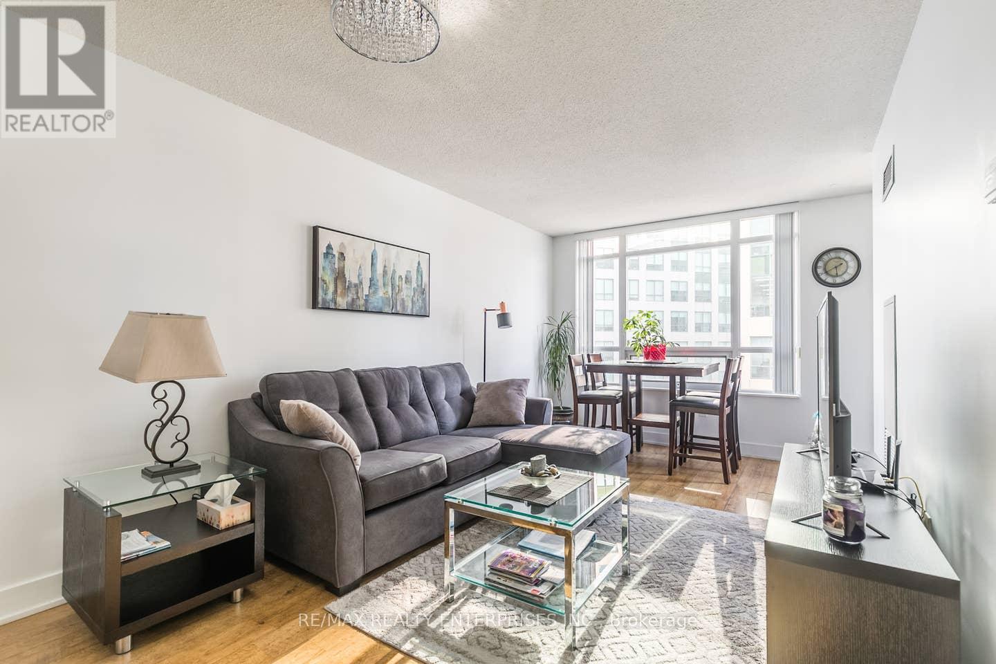 A living room with a grey couch, a glass coffee table, and a lamp on a side table.