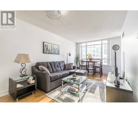 A living room with a grey couch, a glass coffee table, and a lamp on a side table.