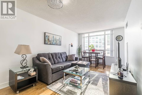 A living room with a grey couch, a glass coffee table, and a lamp on a side table.