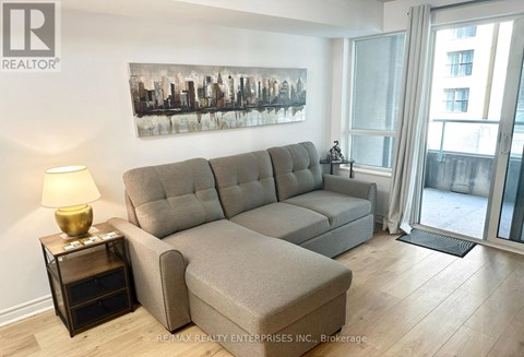 A living room with a grey sofa and a painting on the wall.
