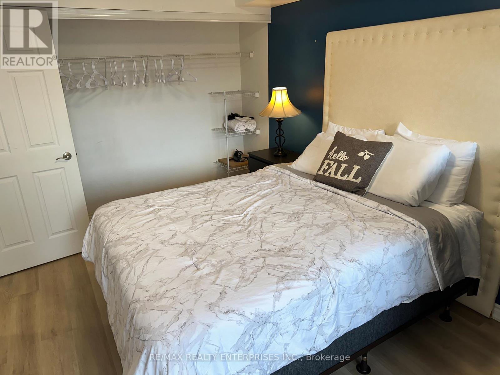 A bedroom with a white bedspread and a grey pillow with the word "FALL" written on it.