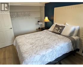 A bedroom with a white bedspread and a grey pillow with the word "FALL" written on it.