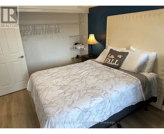 A bedroom with a white bedspread and a grey pillow with the word "FALL" written on it.