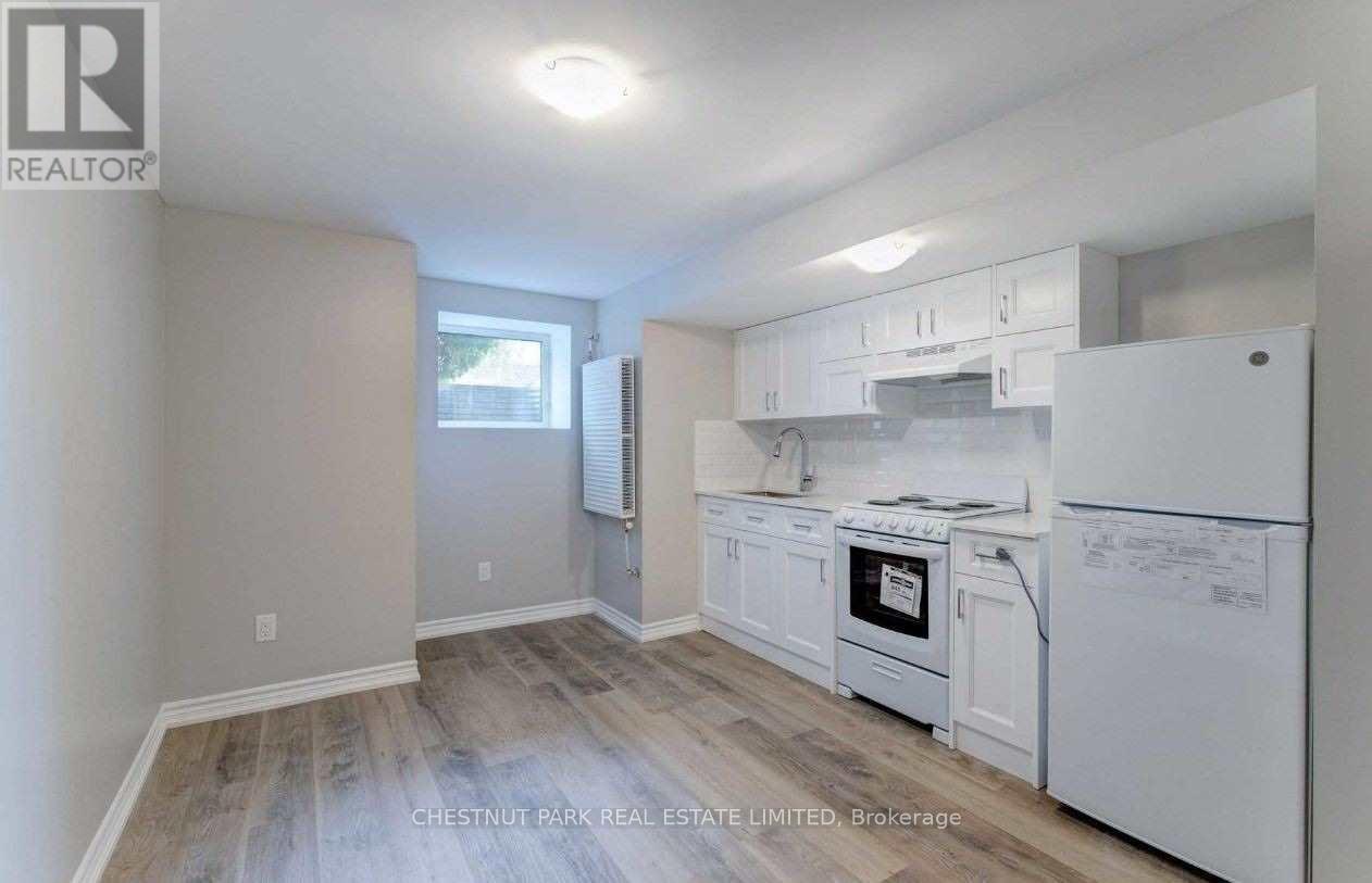 A real estate listing image of a kitchen with white appliances and wood flooring.