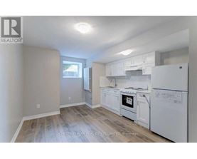 A real estate listing image of a kitchen with white appliances and wood flooring.