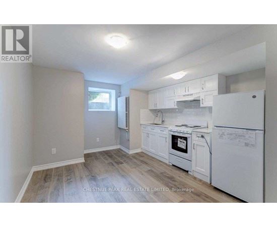 A real estate listing image of a kitchen with white appliances and wood flooring.
