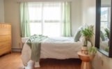 A bedroom with a bed, a nightstand, and a window with green curtains.