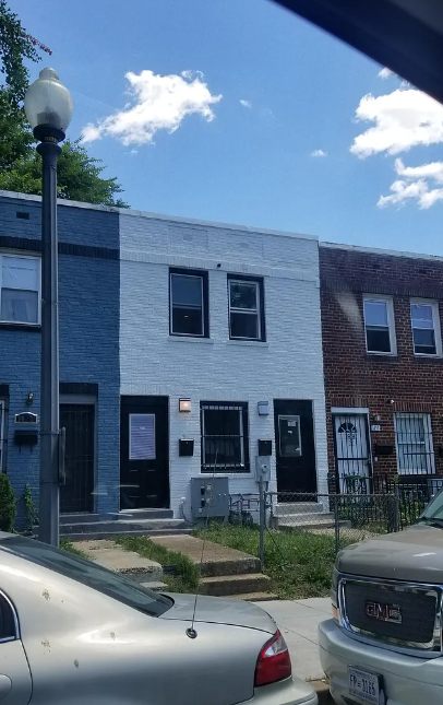 A white car is parked in front of a blue and white building.
