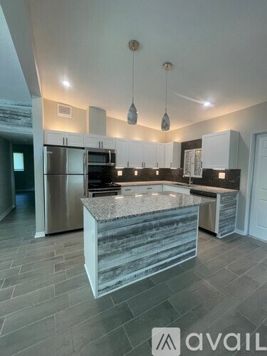 A modern kitchen with a marble island and pendant lights.
