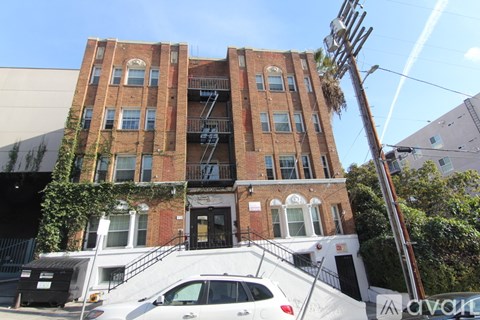 A white car is parked in front of a red brick building.
