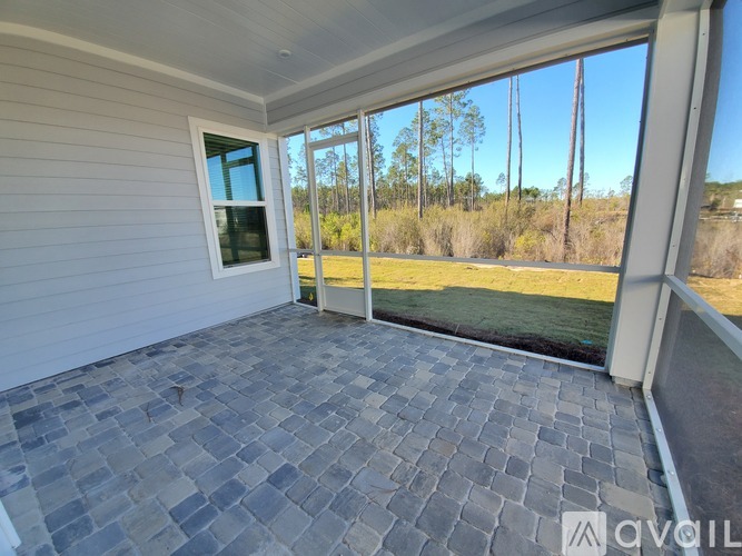 A patio with a grey stone floor and a sliding glass door leading to a grassy area.