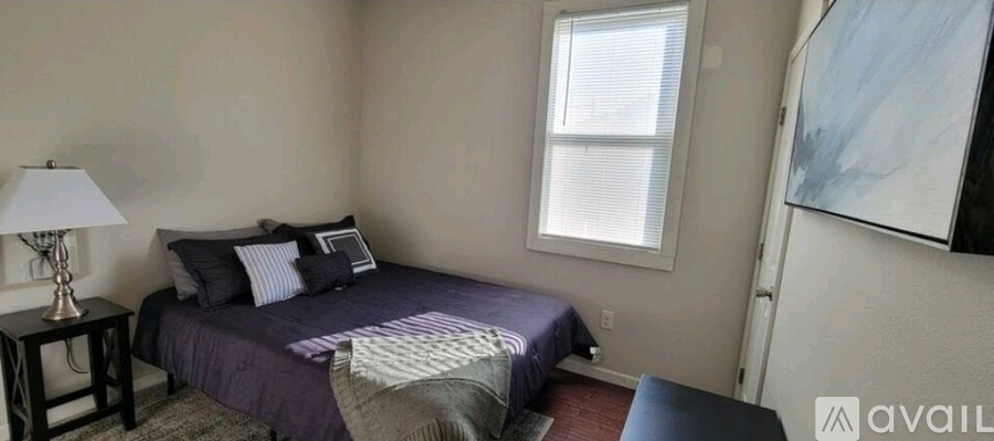A bedroom with a purple bedspread and a white window.