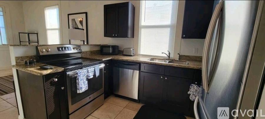 A modern kitchen with black cabinets and a stainless steel refrigerator.