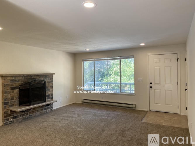 A living room with a fireplace and a window with a view of trees.