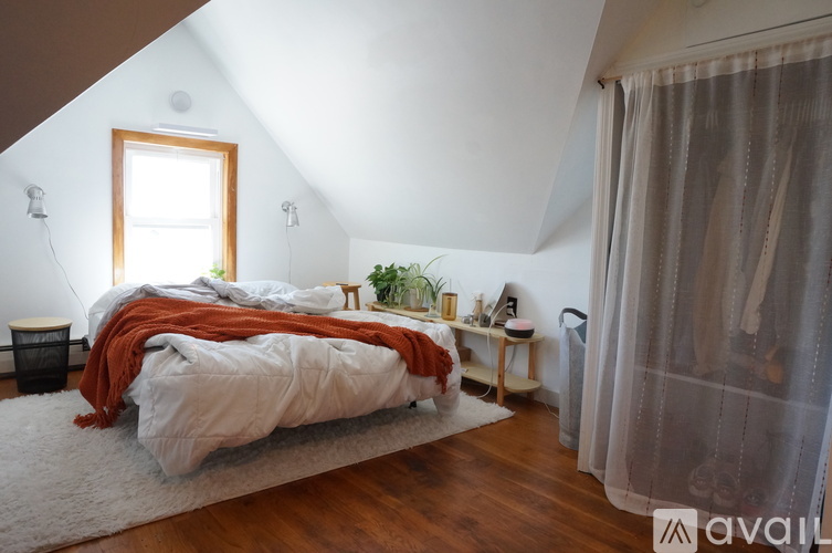 A bedroom with a bed covered in a white comforter and orange blanket.