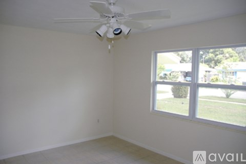 A room with a ceiling fan and a window overlooking a green lawn.