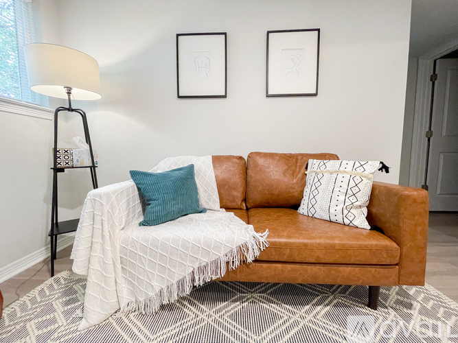 A brown couch with a white throw blanket and two pillows.