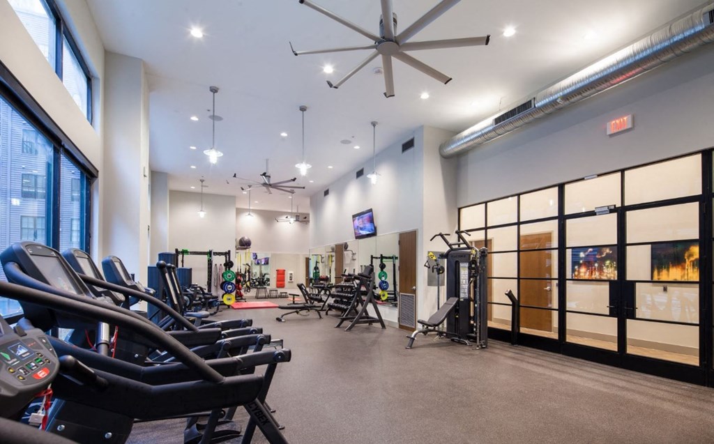 a gym with weights and chairs and a ceiling fan