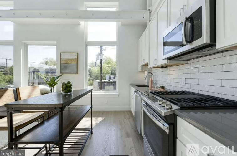A kitchen with a black countertop and stove, a wooden dining table with chairs, and a window with a view of the outdoors.