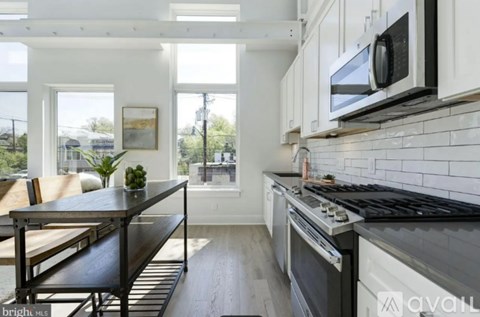 A kitchen with a black countertop and stove, a wooden dining table with chairs, and a window with a view of the outdoors.