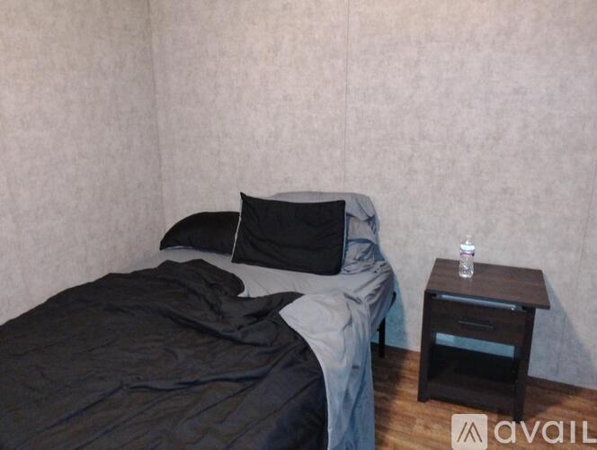 A bed with a grey blanket and two black pillows sits next to a small wooden nightstand.