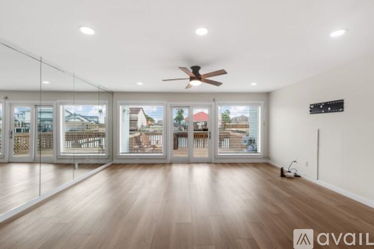 A spacious room with a ceiling fan and large windows overlooking a residential area.