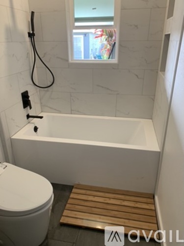A white bathroom with a toilet, a bathtub and a window.