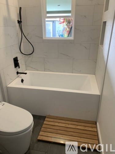 A white bathroom with a toilet, a bathtub and a window.