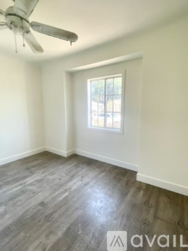 A room with a ceiling fan and a window with a view of a fence and trees.